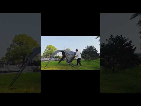 Person setting up a quick-opening dome pop up canopy tent outdoors in a grassy park with trees